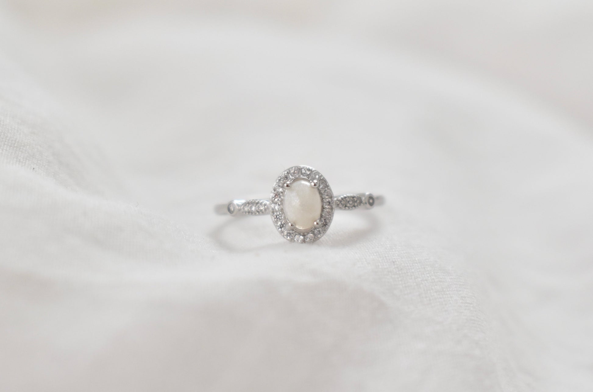 Silver cremation ring with an oval gemstone center and a halo of small sparkling stones, offered as a unique pet memorial jewelry piece.