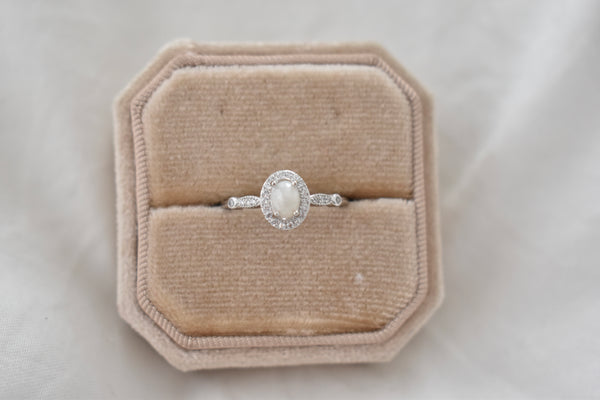Silver or white gold ring with an oval pearl-like center stone and a sparkling halo, presented as a cremation ring or memorial jewelry.