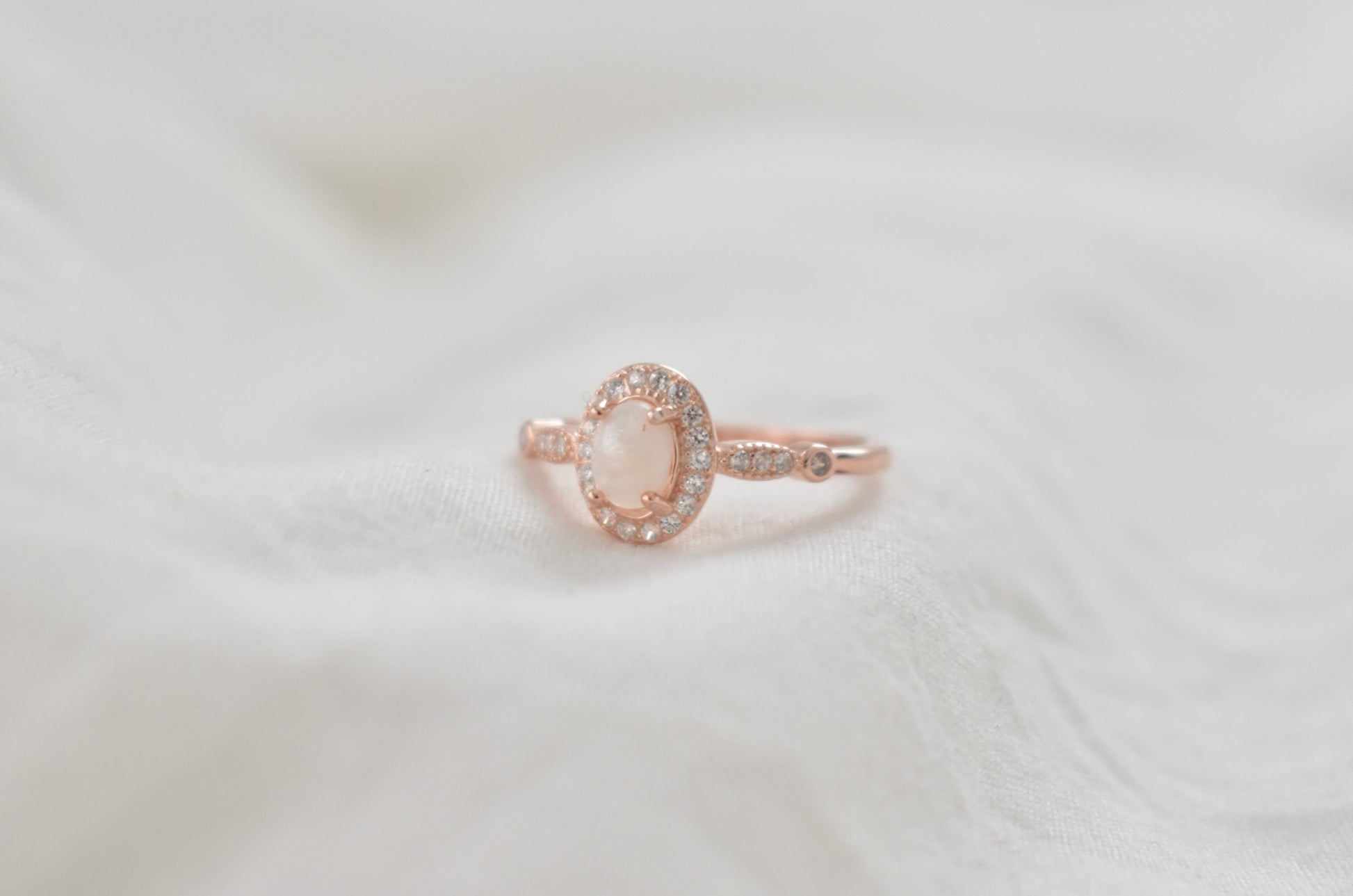 Rose gold ring with an oval cremation gemstone center, surrounded by a sparkling halo of stones, suitable for a memorial jewelry piece.