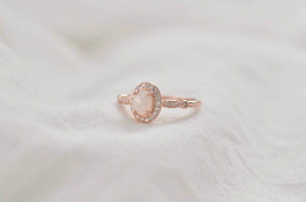 Rose gold ring with an oval cremation gemstone center, surrounded by a sparkling halo of stones, suitable for a memorial jewelry piece.