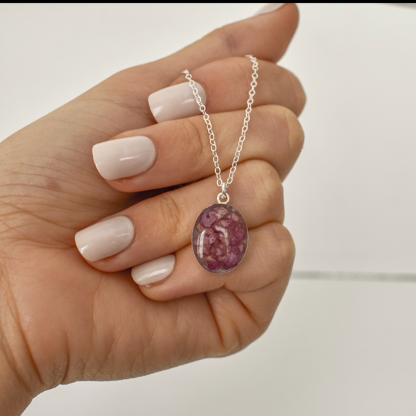 Silver necklace with an oval pendant containing a reddish-pink material, designed as a floral memorial jewelry piece.