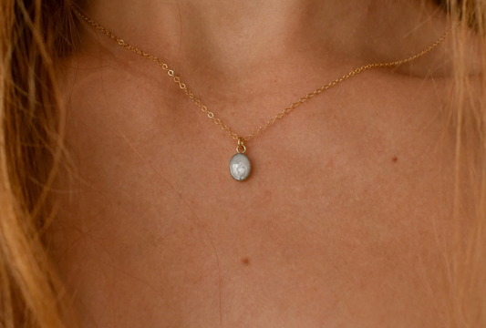 Gold necklace with a small, light-colored oval pendant, designed as a simple keepsake or memorial jewelry piece