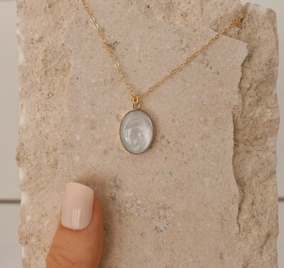 Simple gold chain necklace with an oval pendant containing a light-colored, swirling keepsake material, designed as a cremation jewelry piece