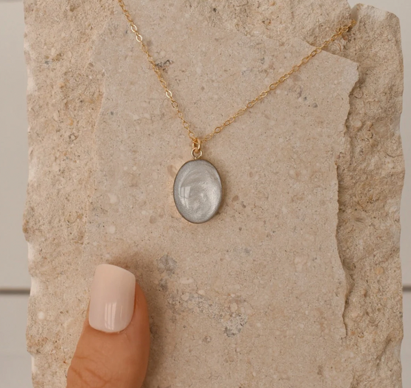 Simple gold chain necklace with an oval pendant containing a light-colored, swirling keepsake material, designed as a cremation jewelry piece