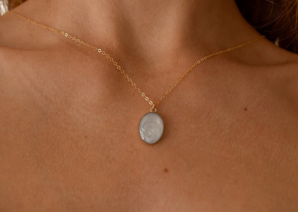 Gold chain necklace with a small, oval pendant containing a pearlescent white keepsake material, designed as a personalized memorial jewelry piece