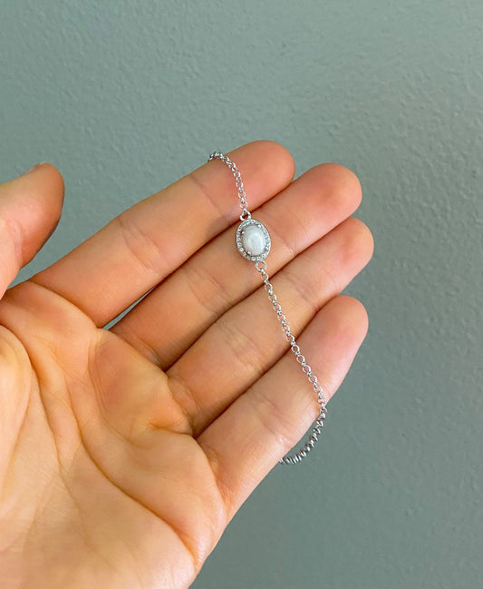 Sterling silver cremation bracelet with an oval white gemstone, surrounded by a halo of smaller stones, a beautiful and simple piece of memorial jewelry
